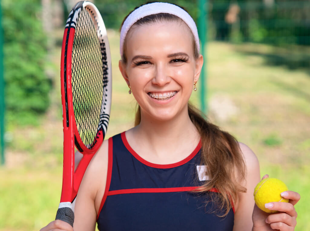 Smiling teen Seapoint patient with braces, holding a tennis racquet